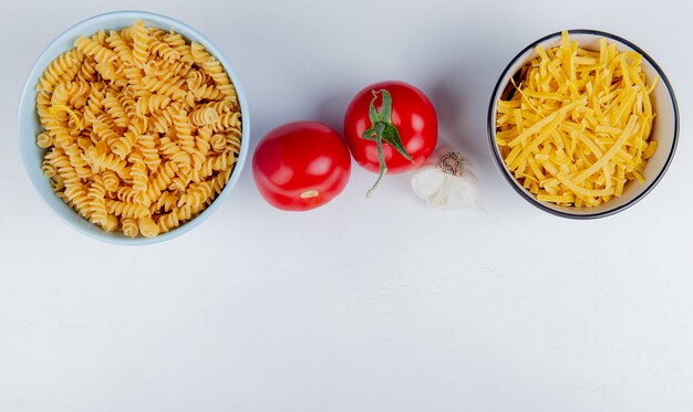 Top view of macaronis as rotini and tagliatelle with tomatoes and garlic on white with copy space