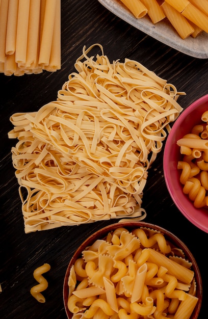 Top view of macaronis as tagliatelle bucatini fusilli and others on wooden surface