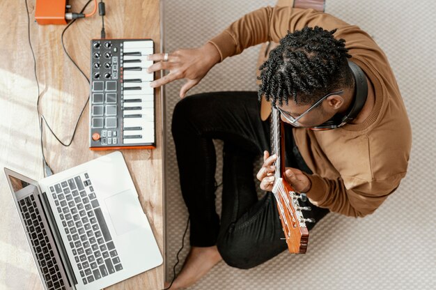 Top view of male musician at home playing guitar and mixing with laptop