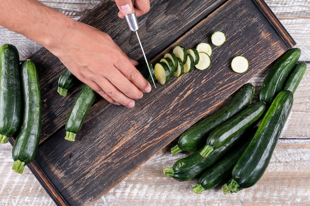 Free photo top view man cutting fresh zucchinis into slices on cutting board on light wooden table