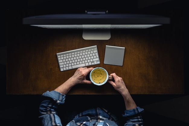 Free photo top view of man working on computer at night holding mug of tea