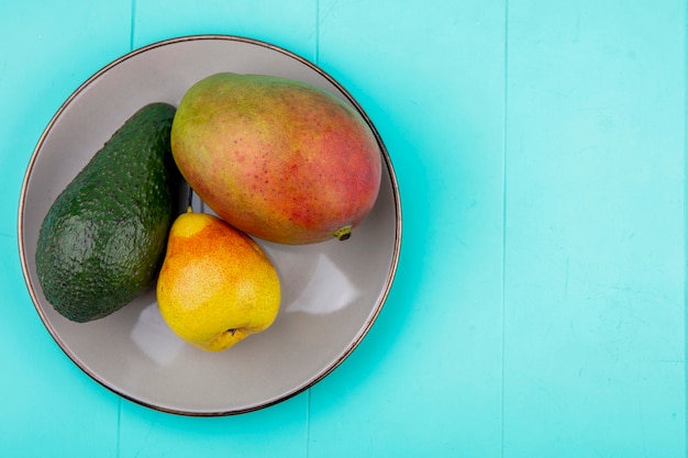 Free photo top view of mango with pear and avocado on a plate on blue surface