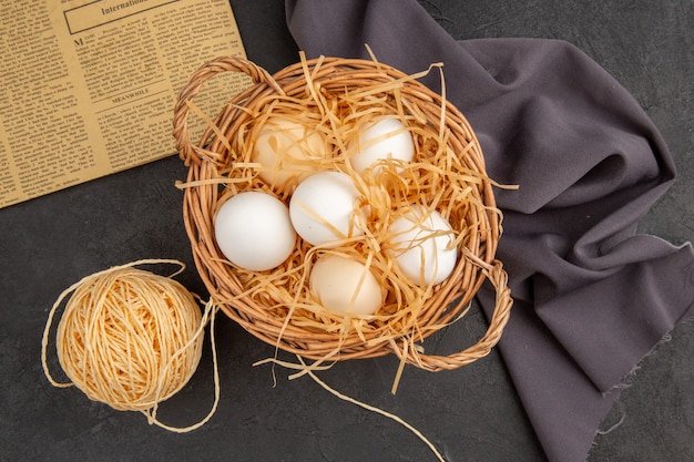 Free photo top view of many organic eggs in a basket on an old newspaper on black towel and rope on dark surface