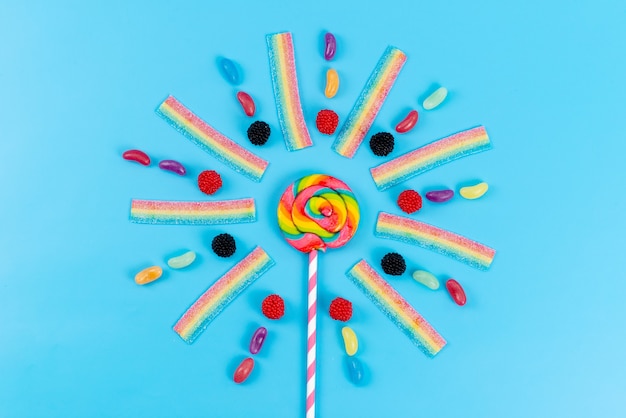 A top view marmalades and lollipops colorful delicious on blue, rainbow color sugar