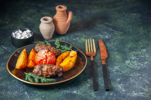 Free photo top view of meat cutlets baked with potatoes and tomato served with green cutlery set salt on dark color background