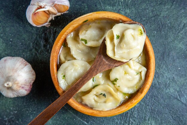 Top view meat dumplings inside wooden plate with oil onion and garlic on dark surface