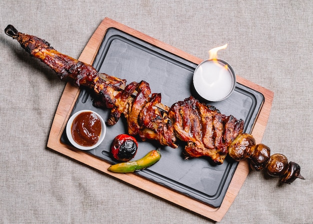 Free photo top view meat kebab on a skewer with grilled potatoes and vegetables with sauce and fire on a board