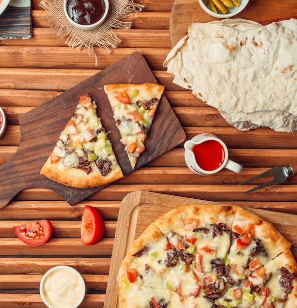 Top view of meat pizza slices on wood cutting board