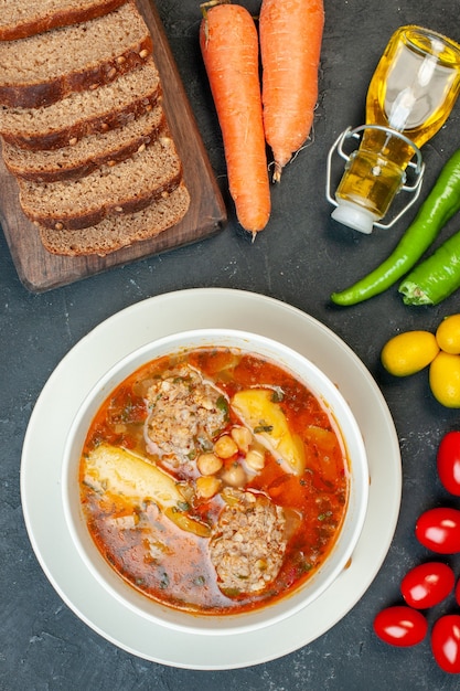 Top view meat soup with bread loafs and seasonings on dark-gray background