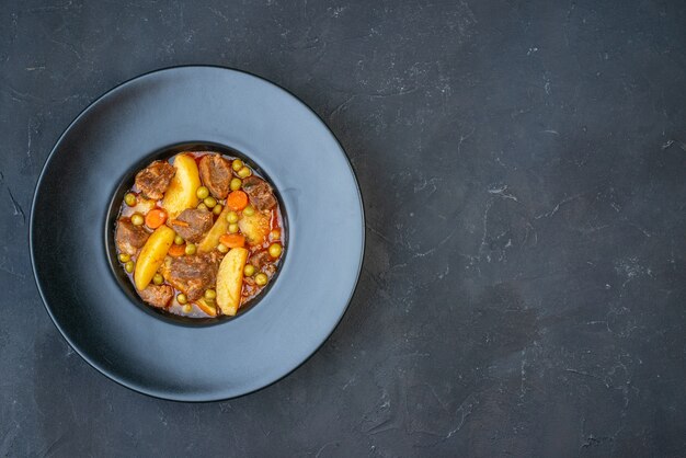 Top view meat soup with garniture on black plate on dark table with free place