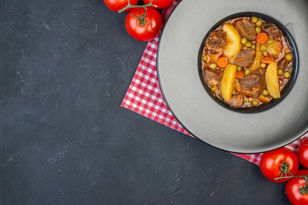 Top view meat soup with garniture on round plate fresh tomatoes on black table with free space