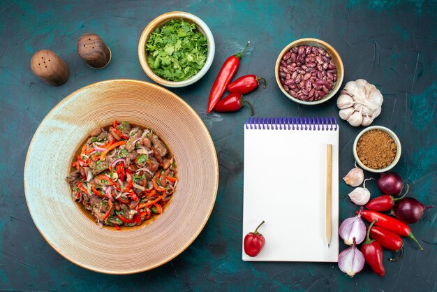 Top view meaty vegetable meal inside plate along with greens peppers beans vegetables with notepad on the dark-blue desk food meal vegetable seasonings