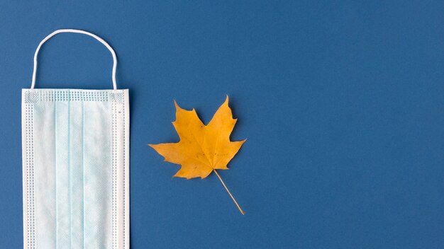 Top view of medical mask with autumn leaf