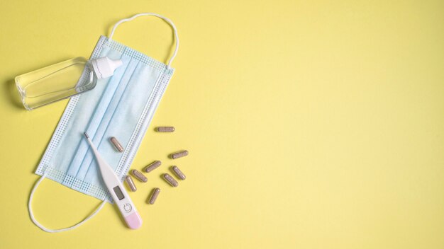 Top view of medical mask with thermometer and pills