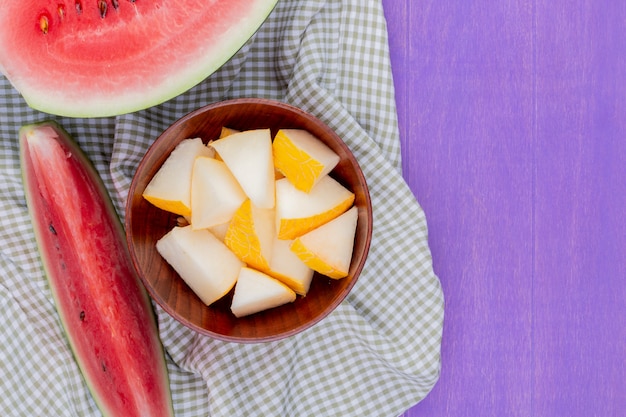 Free photo top view of melon slices in bowl with watermelon half and slice on purple background with copy space