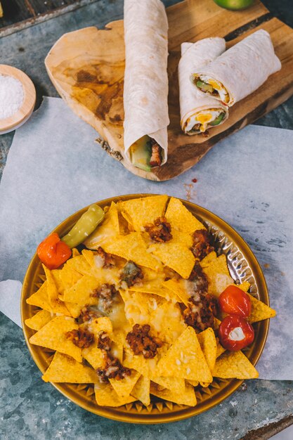 Top view of mexican nachos tortilla chips in plate with mexican tacos on cutting board