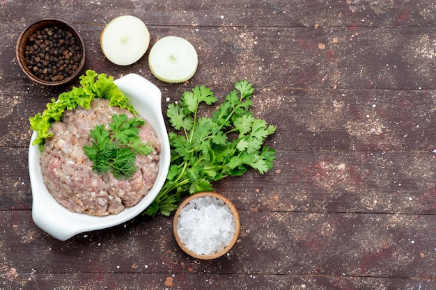 Free photo top view minced raw meat with greens inside plate with onions salt on the brown background meat raw food meal green photo