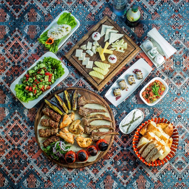 Top view of mixed kebab served with fresh vegetable salad cheese plate and eggplant rolls on a colorful rug