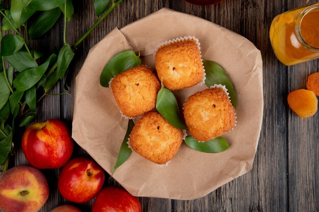 top view of muffins with green leaves on craft brown paper with fresh ripe nectarines on rustic wooden table