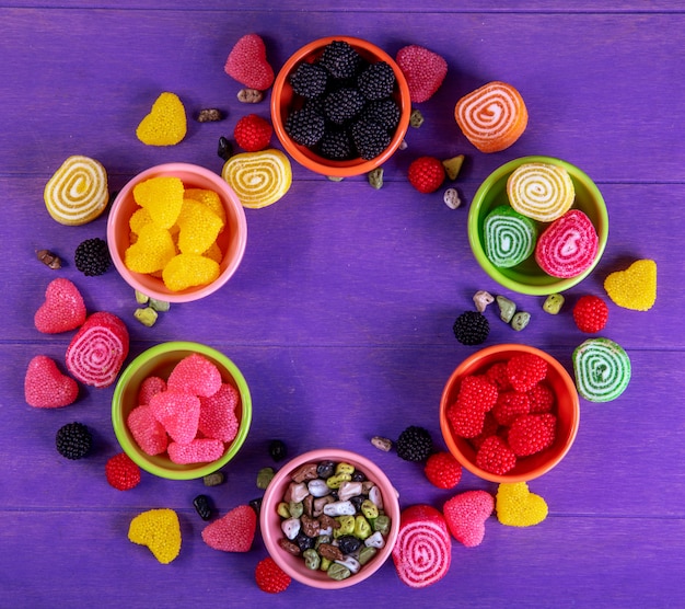 Top view multi-colored marmalade with chocolate stones in saucers for jam on a purple background