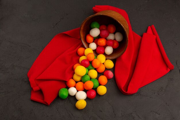 top view multicolored candies sweet inside brown pot on the red tissue and dark