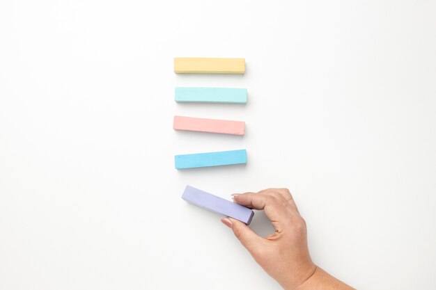 Top view of multicolored chalk and a woman's hand holding one for education day