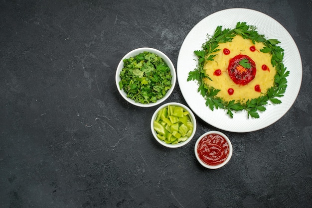 Top view of mushed potato dish with tomato sauce and greens on dark