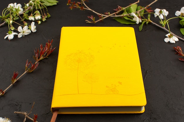 top view mustard copybook around white flowers on the dark