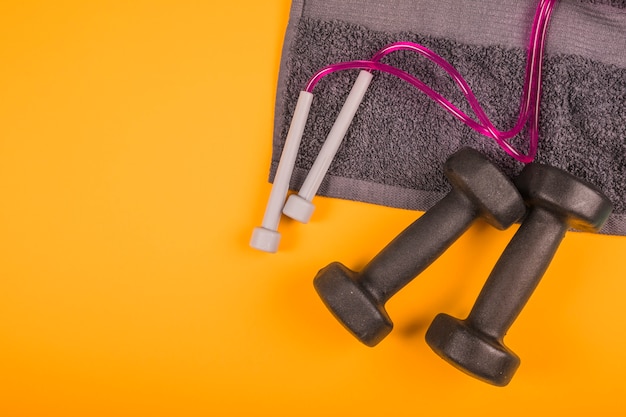 Free photo top view of napkin with skipping rope and black dumbbells on yellow background