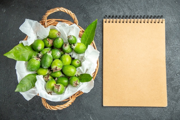 Top view of natural fresh green feijoas with leafs in a brown wricked basket and notebook