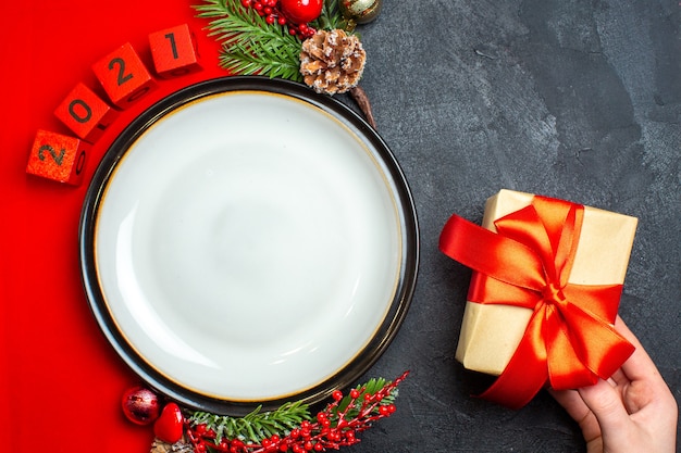 Top view of New year background with dinner plate and gift decoration accessories fir branches and numbers on a red napkin on a black table