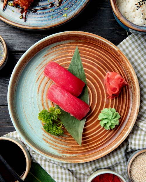 Top view of nigiri sushi with tuna on bamboo leaf served with pickled ginger slices and wasabi on a plate