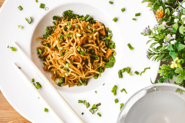 Free photo top view of noodles with chicken and chopped green onion in a white bowl on white background