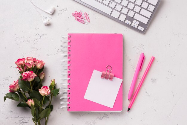 Top view of notebook on desk with bouquet of roses and pens