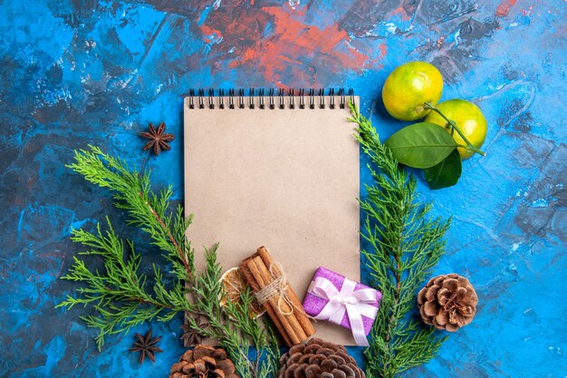 Top view a notebook pine tree branches pinecones anises fresh mandarines on blue background free space