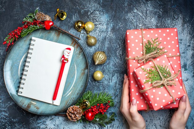 Top view of notebook with pen on blue plate decorative accessories and hand holding a gift box on dark background