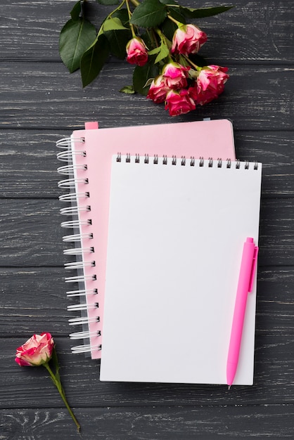 Top view of notebooks on wooden desk with bouquet of roses