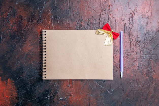 Top view a notepad with little bow pen on dark red background with copy place