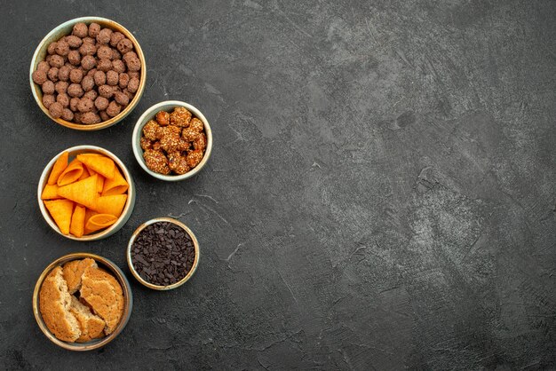 Top view nuts and chips inside little pots on dark-grey desk color snack chip