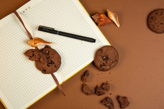 Free photo top view of oatmeal cookies with chocolate chips and open empty notebook with pen on ocher