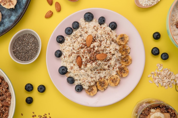 Top view of oatmeal with banana blackthorn almond flax in plate with oat chia seeds on yellow background