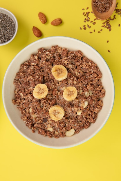 Top view of oatmeal with banana walnut in bowl with almond sesame on yellow background