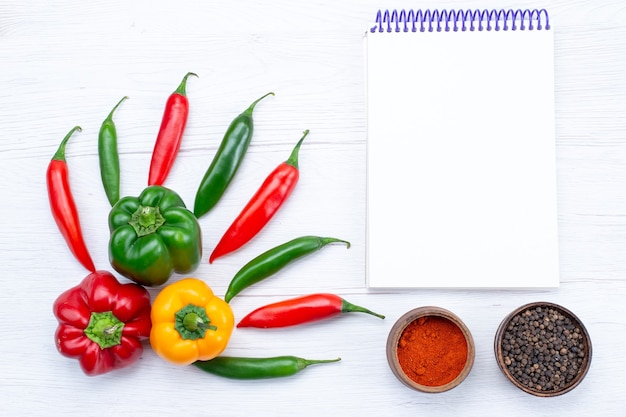 Free Photo top view offul bell-peppers with spicy peppers notepad seasonings on white desk,  vegetable spice hot food meal ingredient product