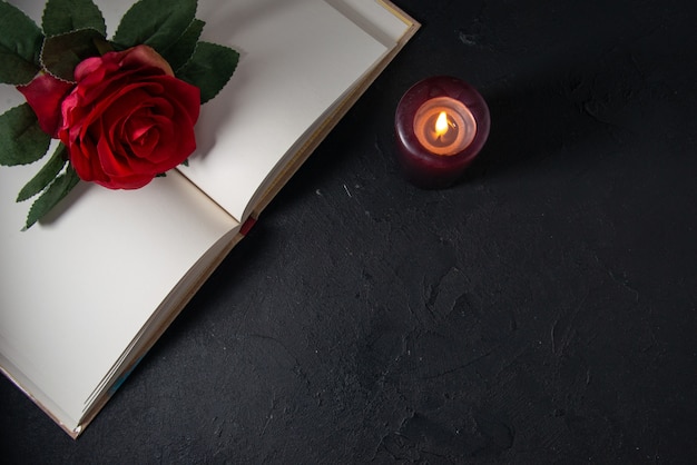 Top view of open book with candle and red flower on dark wall