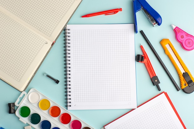 Top view open copybook with colorful paints on ice blue surface