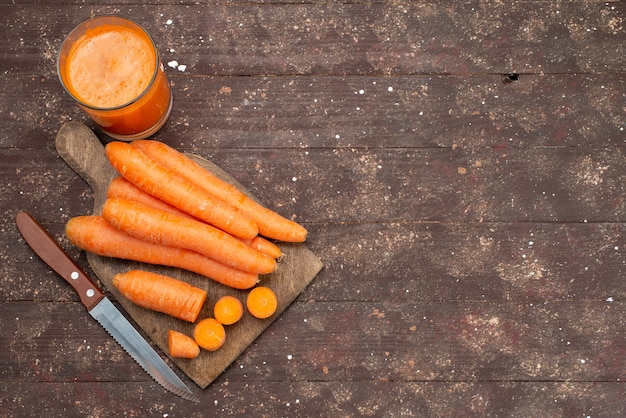 Top view orange carrots sliced and whole with fresh carrot juice on brown