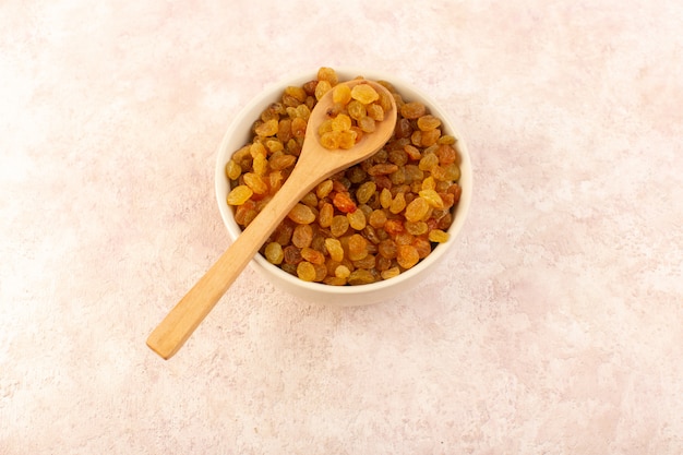 A top view orange dried raisins inside white round plate with wooden spoon on pink