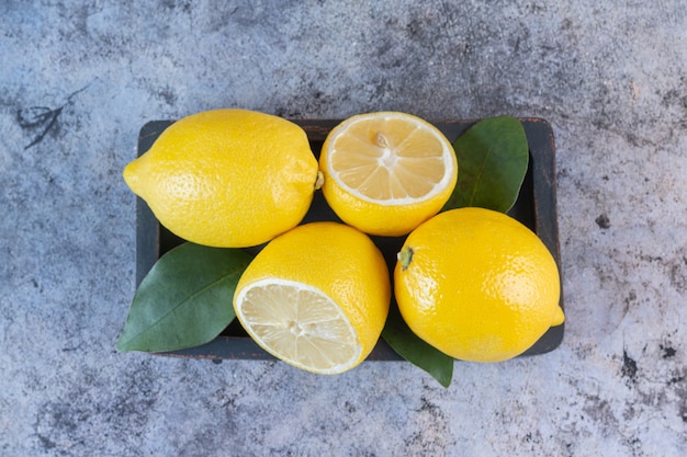 Top view of organic juicy lemons on wooden plate over grey.