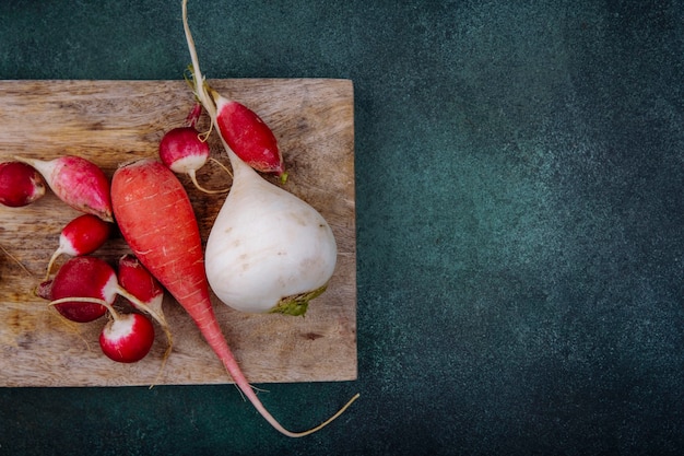 Free photo top view of organic white and pinkish red root vegetable beetroots on a wooden kitchen board with radishes on a green surface with copy space