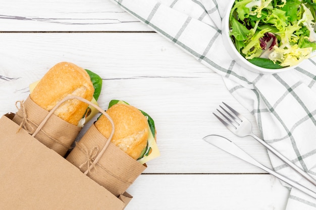 Top view of paper bag with two sandwiches inside and salad